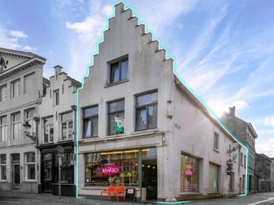 Hoekgebouw met verhuurde winkelruimte en duplex appartement op drukke invalsweg te Brugge.