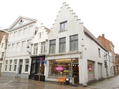 Hoekgebouw met verhuurde winkelruimte en duplex appartement op drukke invalsweg te Brugge.